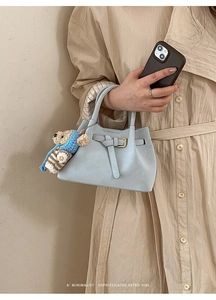 Detail of light blue crossbody bag with a plush bear charm and buckle strap decor