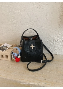 Close-up of black lychee grain leather bucket bag with a cute teddy bear charm
