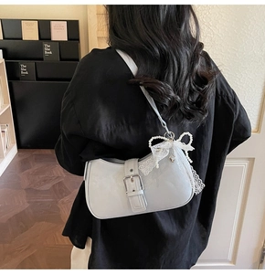 Detail of grey half-moon shoulder bag featuring a white lace bow and pearl heart charm