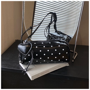 Detail of black polka dot cylinder shoulder bag with a leather heart pendant accessory