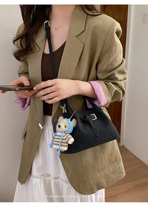 Detail of black crossbody bucket bag with decorative buckle and bear charm accessory