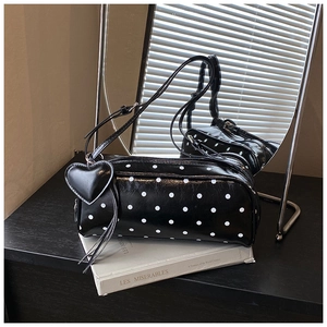 Close-up of a glossy black polka dot cylinder bag with a heart charm and strap