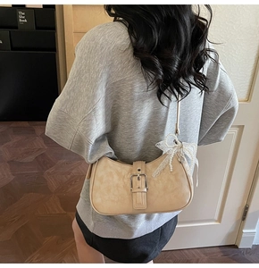 Detail view of beige hobo bag with vintage texture, metal buckle and lace pearl bow charm