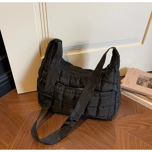 Detailed view of black quilted dumpling bag with adjustable strap on wooden floor