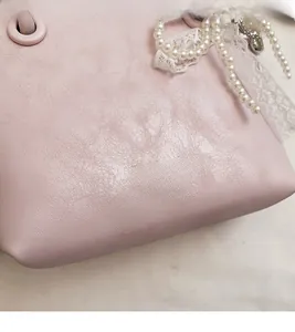 Détail du sac en cuir rose grainé avec pendentif en perles et nœud en dentelle blanche