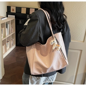 Detail view of pink wrinkled patent leather tote bag with a white horse charm