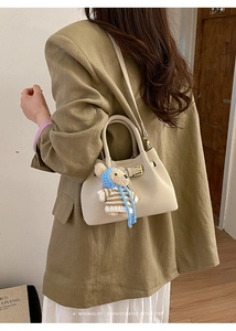 Detail view of cream leather crossbody bucket bag with retro metal strap and cute bear charm