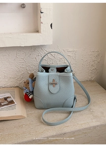 Detail of light blue textured bucket bag with metal buckle and cute bear charm