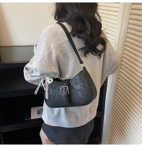 Detail of black textured faux leather bag featuring a silver buckle and lace pearl charm