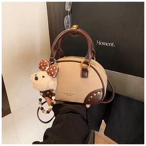 Detail of two-tone beige and brown leather bowling bag with gold studs and bear charm
