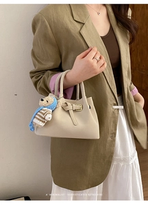 Detail of cream white retro bucket bag with cute bear charm on green blazer and lace skirt