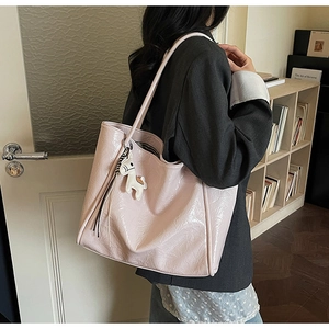 Detail of light pink large capacity tote bag with cartoon horse charm worn with a blazer