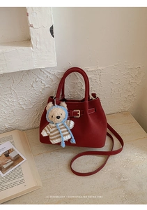 Detail of burgundy leather bucket bag with a cute bear charm in a retro setting