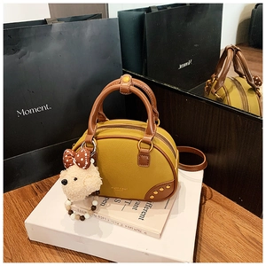 Close-up of yellow Boston bag with brown trim and cute white plush puppy charm