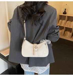 Detail view of white half-moon shoulder bag with decorative metal buckle and pearl charm