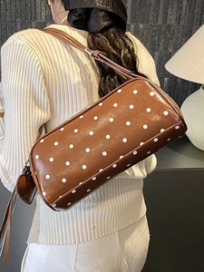 Brown polka dot barrel shoulder bag with heart charm shown on model in cozy interior