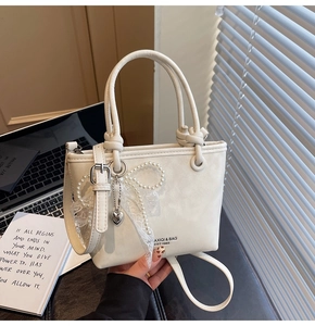 Détail du sac seau crème montrant le cuir texturé avec nœud en perles et breloque