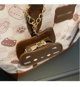 Dettaglio di borsa tote bianca con stampa gatto, etichetta in pelle e ciondolo portamonete