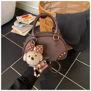 Detail view of brown faux leather pillow bag with gold rivets and cute poodle charm