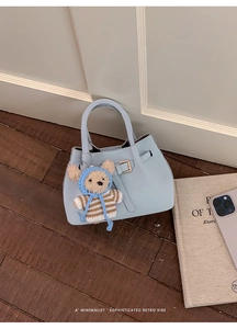 Detail of light blue faux leather bucket bag with gold hardware and teddy bear charm