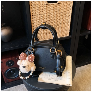 Close-up of black lychee leather handbag with gold hardware and plush bear charm