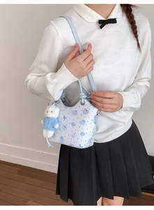 Detail view of light blue crossbody bucket bag with cartoon prints and plush bear charm
