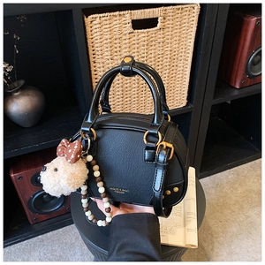 Detail of black lychee grain leather pillow bag with gold hardware and plush puppy charm