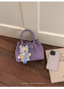 Purple retro bucket bag with decorative buckle and cute teddy bear charm on wood floor
