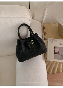 Close-up of black retro bucket bag with matte litchi texture and golden buckle detail