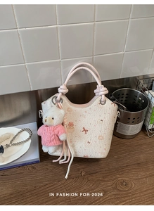 Close-up of white leather bucket bag with pink handle and a cute teddy bear charm