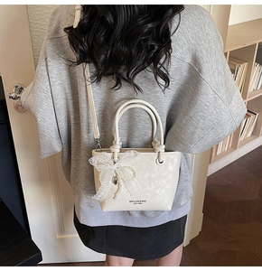 Détail du sac seau crème avec nœud en dentelle, breloque perle et bandoulière amovible