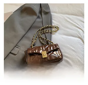 Detail of brown quilted crossbody bag with gold twist lock on grey blazer backdrop