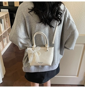 Détail d'un mini sac seau crème avec nœud en dentelle et perle porté par un mannequin