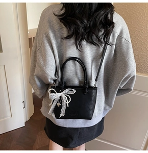 Détail d'un sac seau noir avec nœud en dentelle blanche et pendentif coeur en perles mates