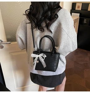 Détail du sac seau noir en cuir avec un nœud en dentelle blanche et des breloques en perles