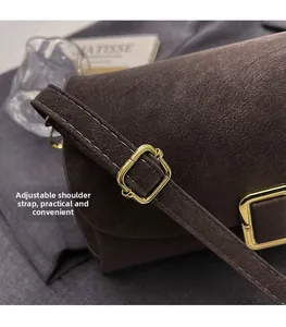 Détail d'une bandoulière réglable avec boucle dorée carrée sur un sac en daim marron foncé