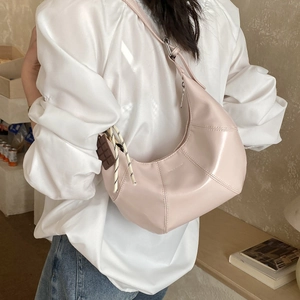Pink crescent shoulder bag with chocolate charm and woven zipper detail in soft lighting