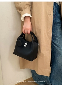 Detail of black pebbled leather bucket bag with silver rotating clasp held by a model