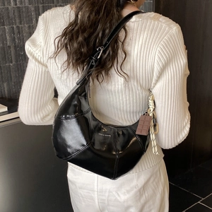 Glossy black crescent shoulder bag with silver buckle and decorative charms on a model