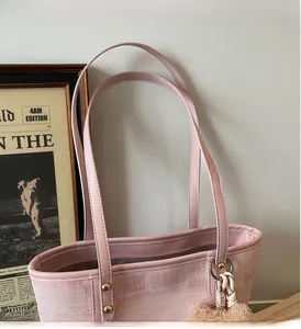 Close-up of pink tote bag showing leather handles, gold rivets and plush charm detail