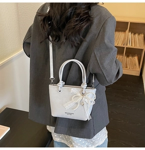 Détail du sac seau bleu clair avec un nœud en dentelle blanche et un pendentif perle
