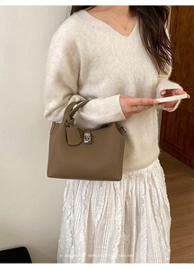 Close-up of minimalist dark brown lychee leather bucket bag with silver buckle and tag