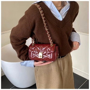 Detail of burgundy quilted crossbody bag with gold chain strap on a brown sweater