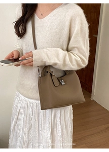 Detail view of beige lychee leather bucket bag with silver clasp on a white sweater outfit