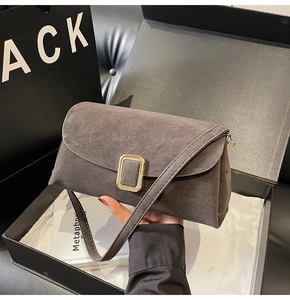 Détail du sac à main en daim gris avec fermoir rectangulaire doré dans une boîte de luxe
