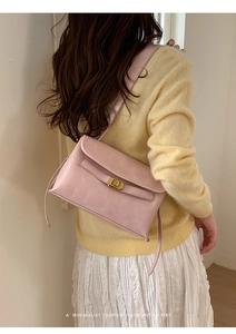 Détail du sac bandoulière rose clair avec fermoir doré porté à l'épaule par un mannequin