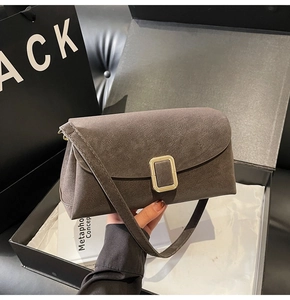 Détail d'un sac à bandoulière en daim café avec boucle dorée dans un coffret