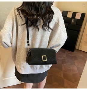 Gros plan d'un sac bandoulière noir avec boucle dorée porté par un mannequin féminin