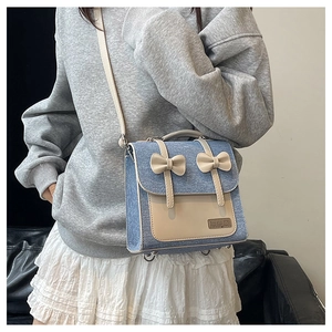 Detailed close-up of light blue denim crossbody bag with cream leather bows and metal feet