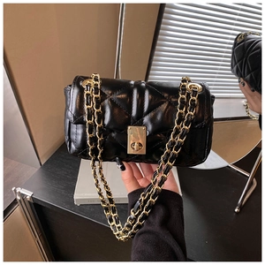 Detail of black quilted crossbody bag showing golden chain strap and turn-lock closure